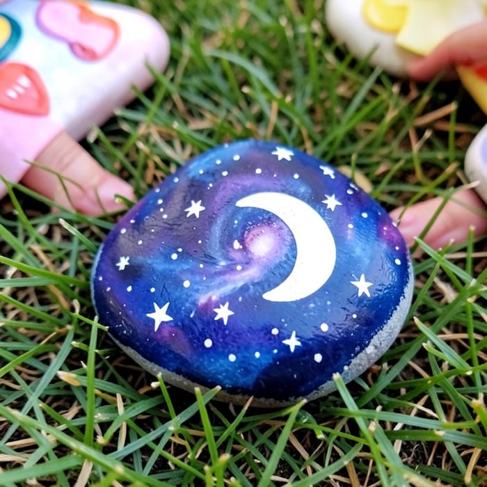 A rock painted with a galaxy, moon and stars